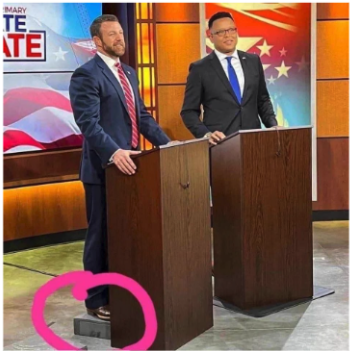 Two candidates for a senitorial debate stand at a podium. One is standing on a step-stool to appear taller